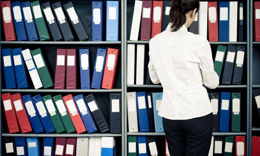 standing in front of shelves filled with colorful office binders